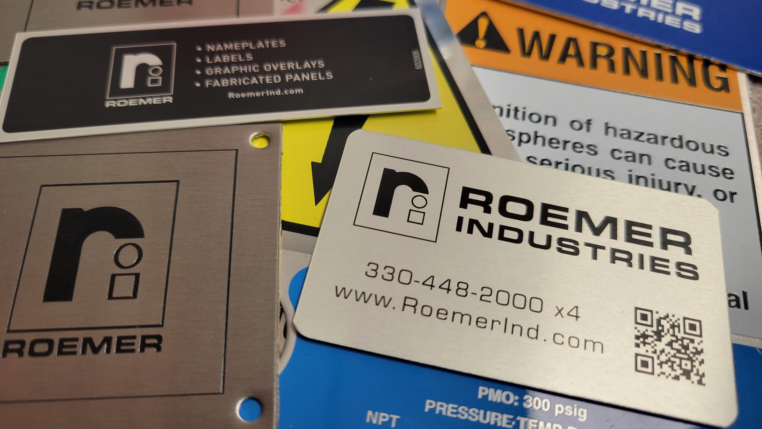 Metal machine safety warning plate with color fills alongside industrial rating nameplates